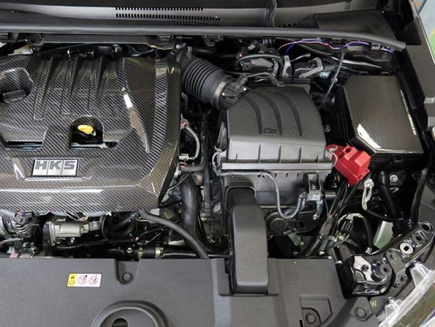 HKS 2023 Toyota GR Corolla dry carbon engine fuse box cover showing sleek carbon fiber design on engine bay.