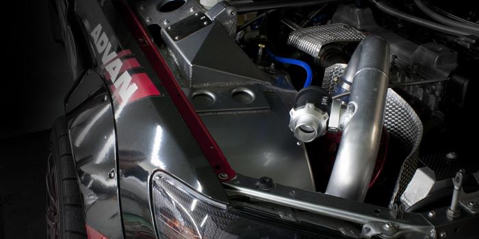 HKS Racing SQV universal blow off valve installed on a turbocharged engine, showcasing its sleek black design and metal components.